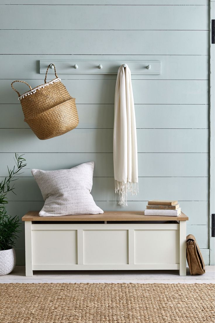 a white bench sitting next to a wall with a basket hanging on it's side