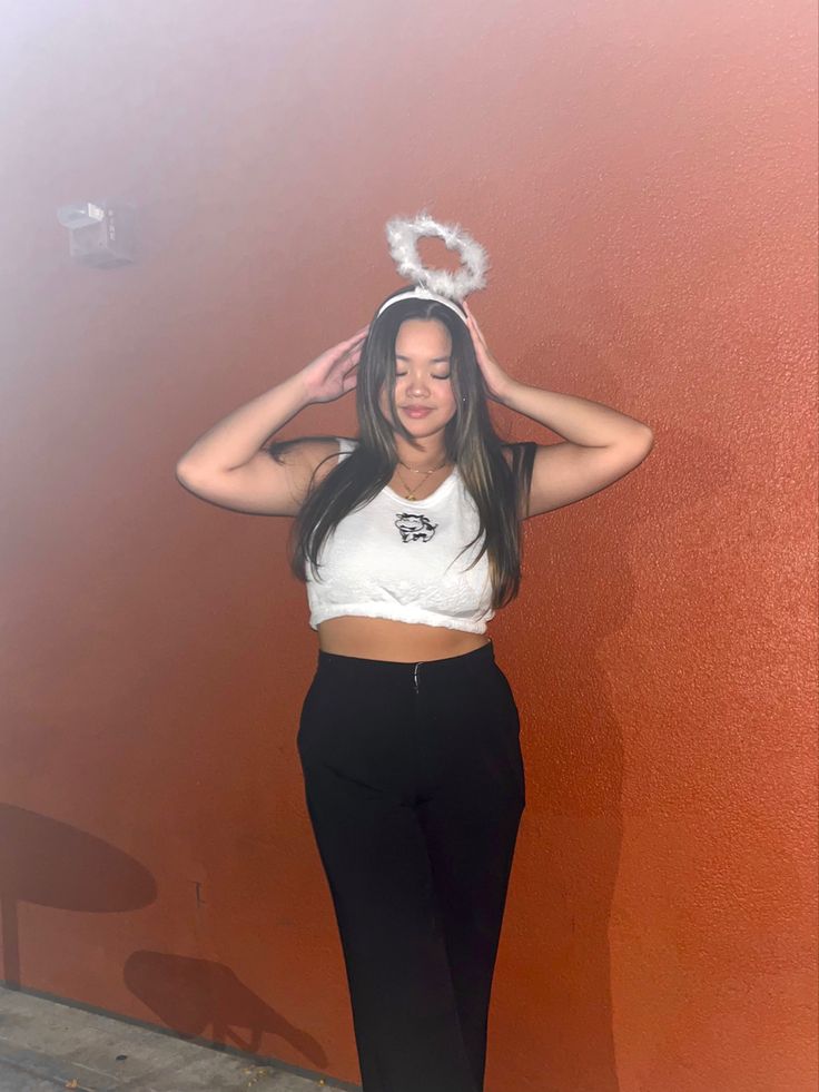 a woman standing in front of a red wall wearing black pants and a white crop top