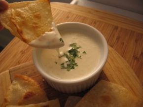 a person dipping some food into a small white bowl on a wooden table with tortilla chips