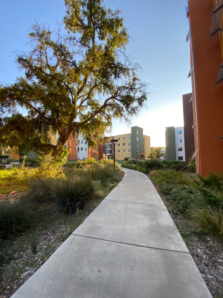 a sidewalk that is in front of some buildings and trees on the other side of the walkway