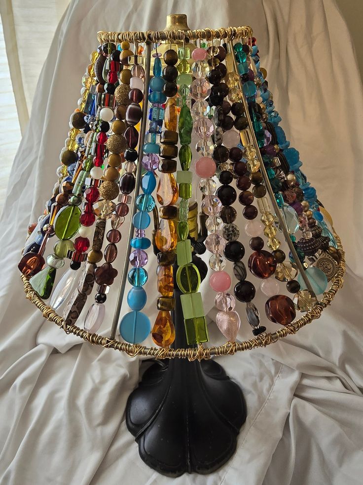 a lamp that has many different colored beads on it and is sitting on a white sheet