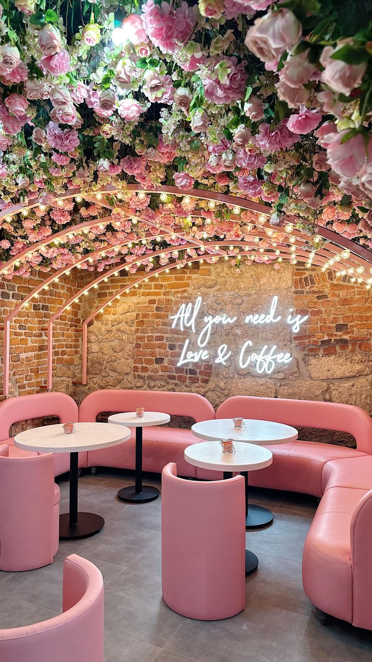 the inside of a restaurant with pink furniture and flowers hanging from the ceiling above it