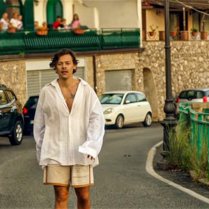 a man in white shirt and tan shorts riding a skateboard on street next to cars