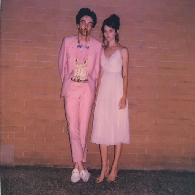 two people standing next to each other in front of a brick wall wearing pink outfits