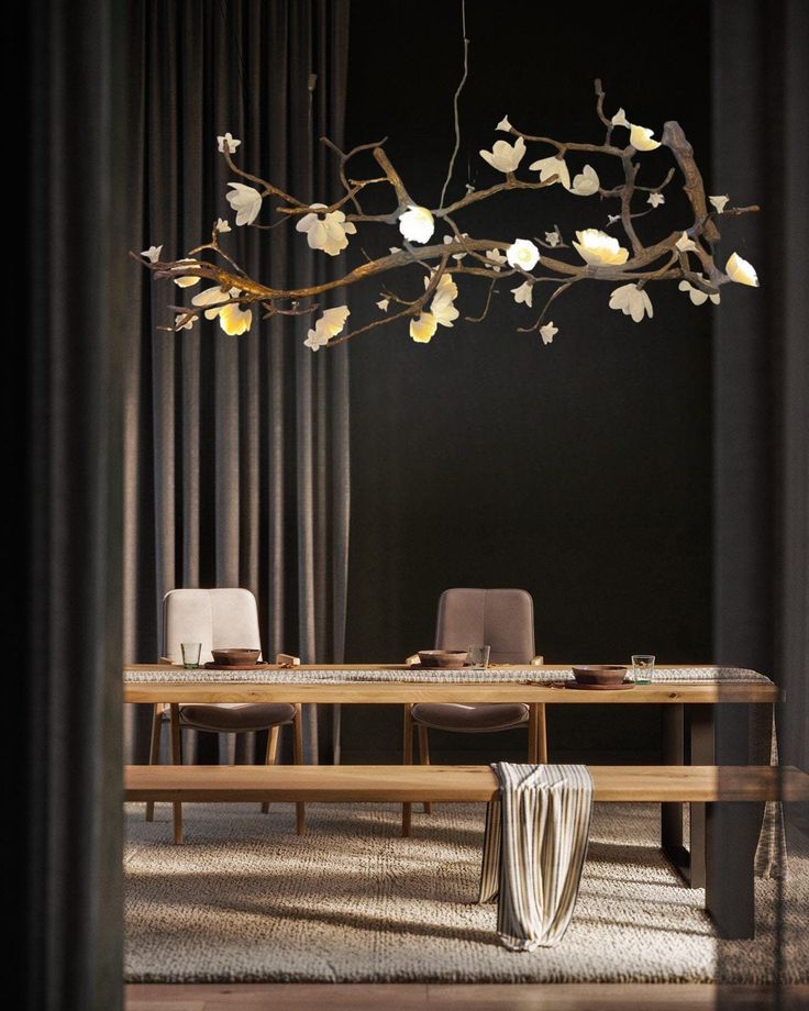 a dining room table and chairs with flowers hanging from the branches above it, in front of curtains