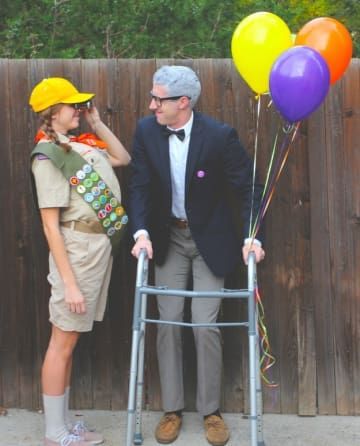 a man and woman dressed up in costumes standing next to a ladder with balloons on it