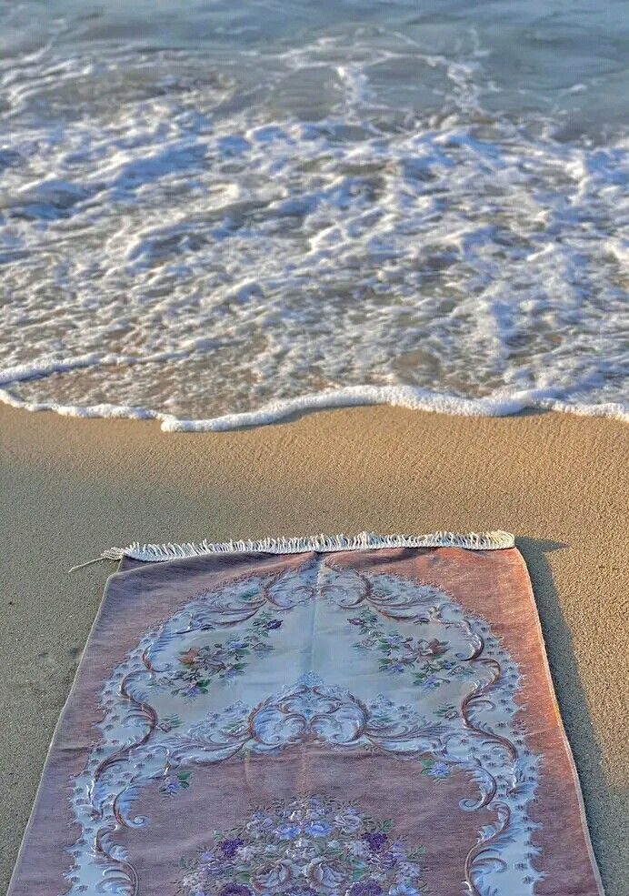 a beach towel is laying on the sand near the ocean water and waves are coming in