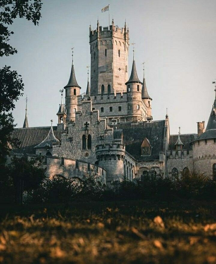 an old castle with turrets and spires is seen from the grass in front of it