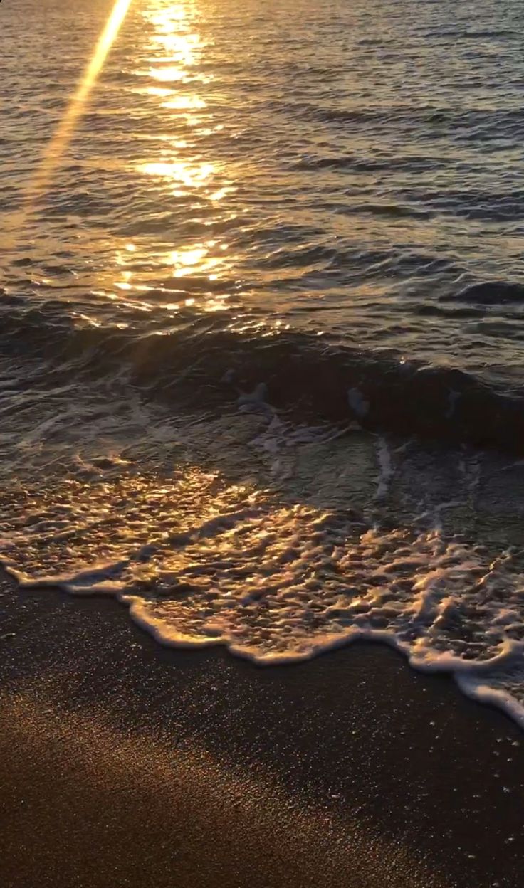 the sun is setting over the ocean with waves coming in to shore and sand on the beach