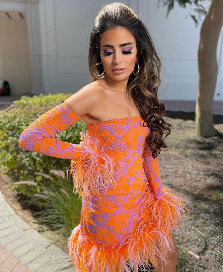 a woman wearing an orange and purple dress with feathers on her body, posing for the camera