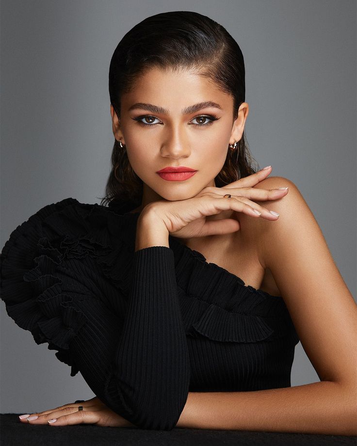 a beautiful young woman sitting at a table with her hand on her chin and looking off to the side