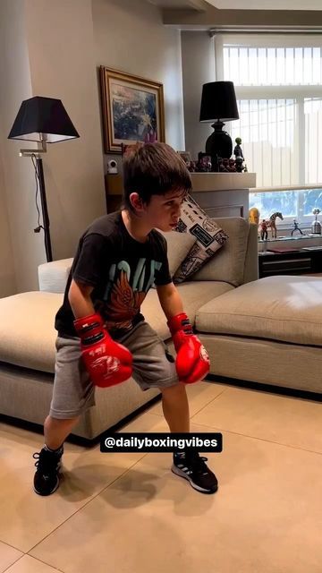 a young boy wearing red boxing gloves sitting on a couch in a living room next to a window