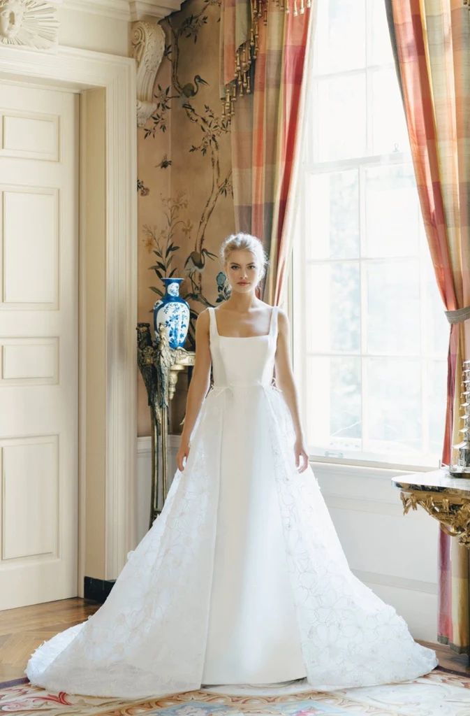 a woman in a white wedding dress standing next to a window with curtains on it