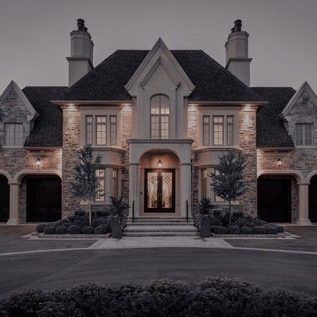 a large house that has lights on in front of it and bushes around the entrance