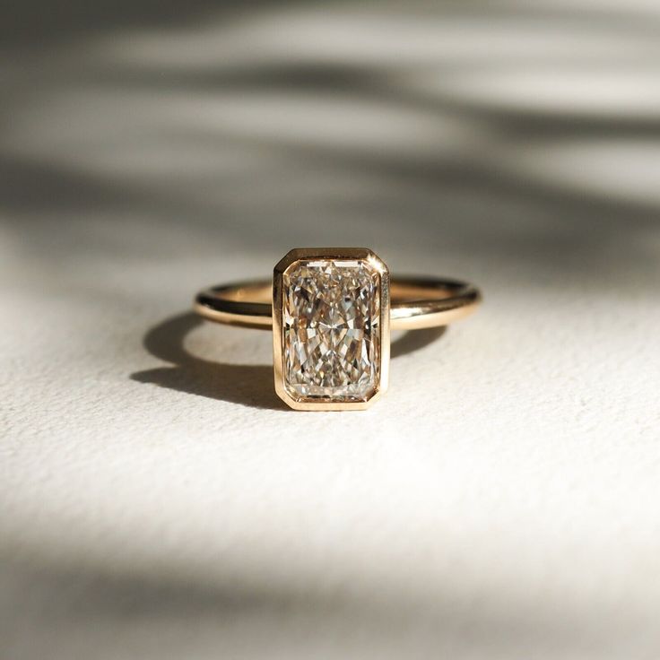 a close up of a diamond ring on a white surface with shadows in the background