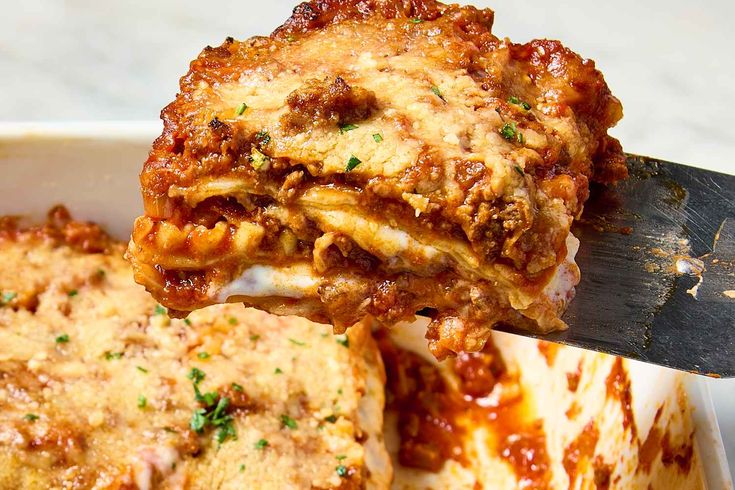 a spatula is lifting up some lasagna from a casserole dish