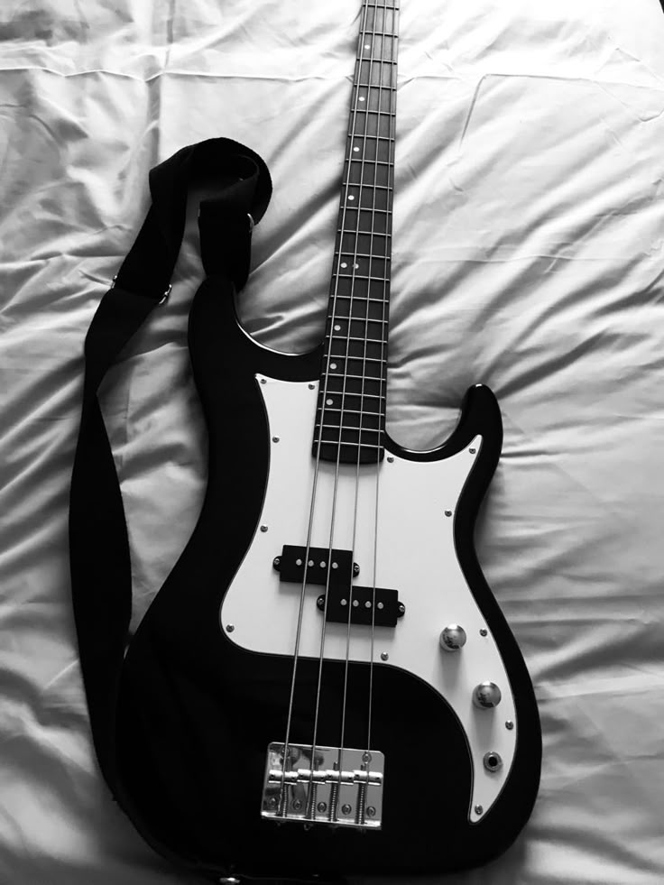 a black and white photo of a bass guitar laying on a bed with its strap around it's neck