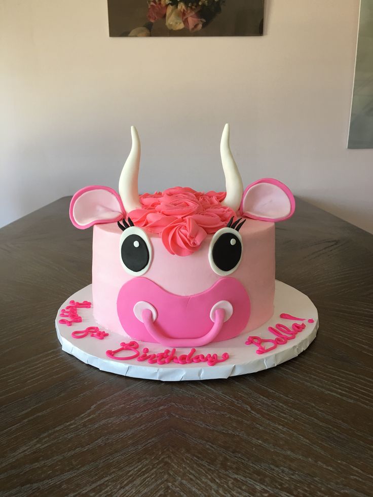 a pink cake decorated with an animal's face and flowers on top is sitting on a table