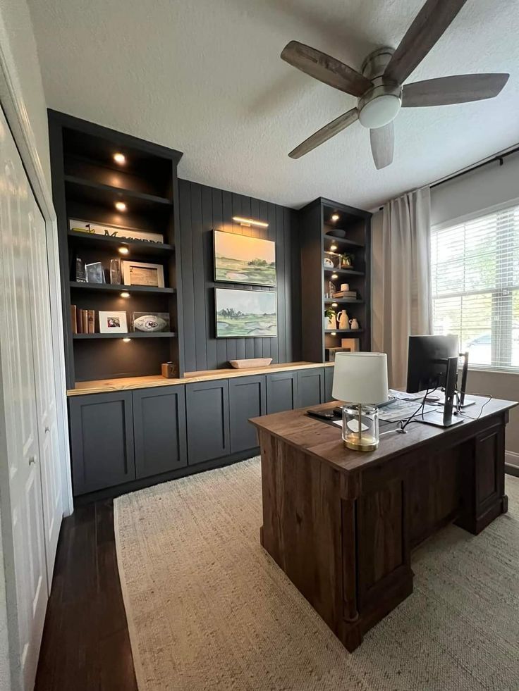 a home office with built in bookcases and a ceiling fan