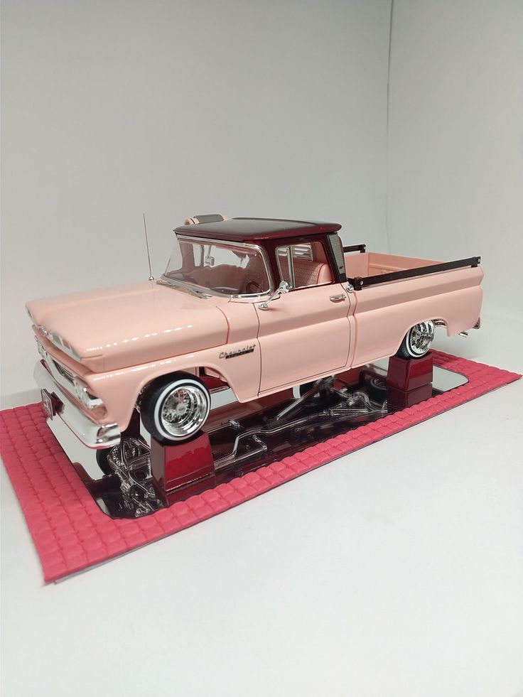 an old model pink truck on display in a white room with a red mat underneath it