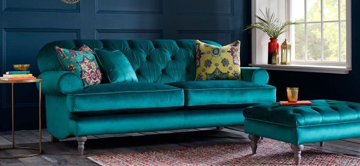 a teal couch and ottoman in a living room with blue walls, rugs and windows