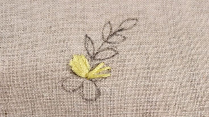 a small yellow flower sitting on top of a piece of linen covered in embroidery thread