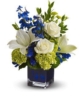 blue and white flowers in a square vase with greenery on the side, including roses