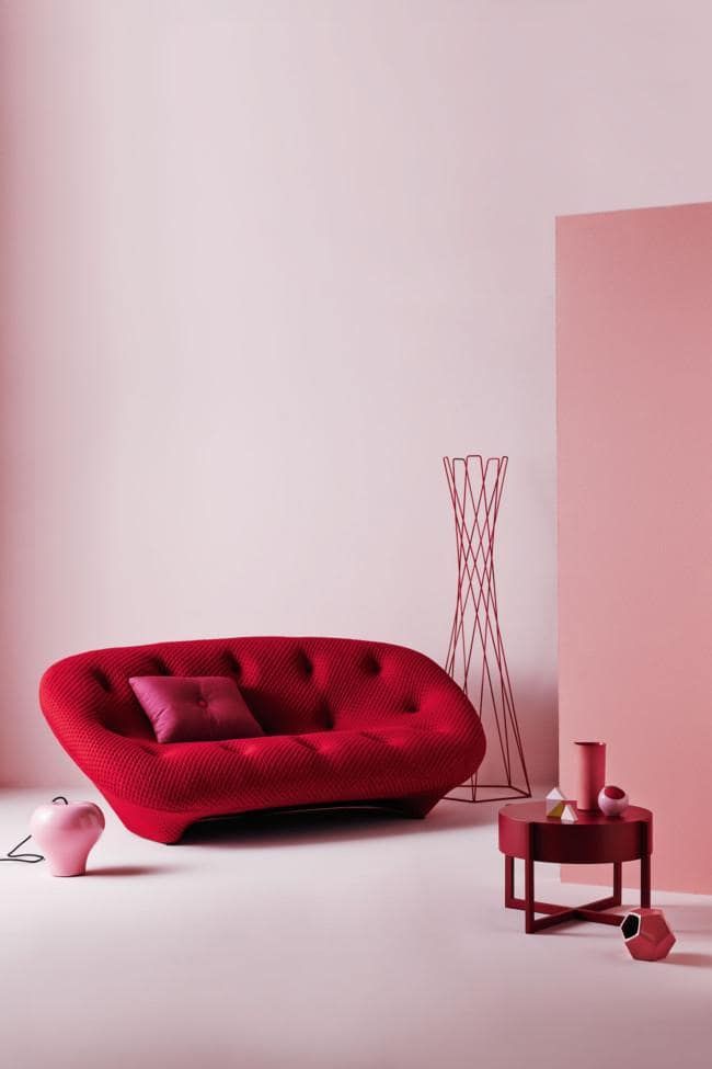 a red couch sitting next to a pink table and chair in a room with white walls