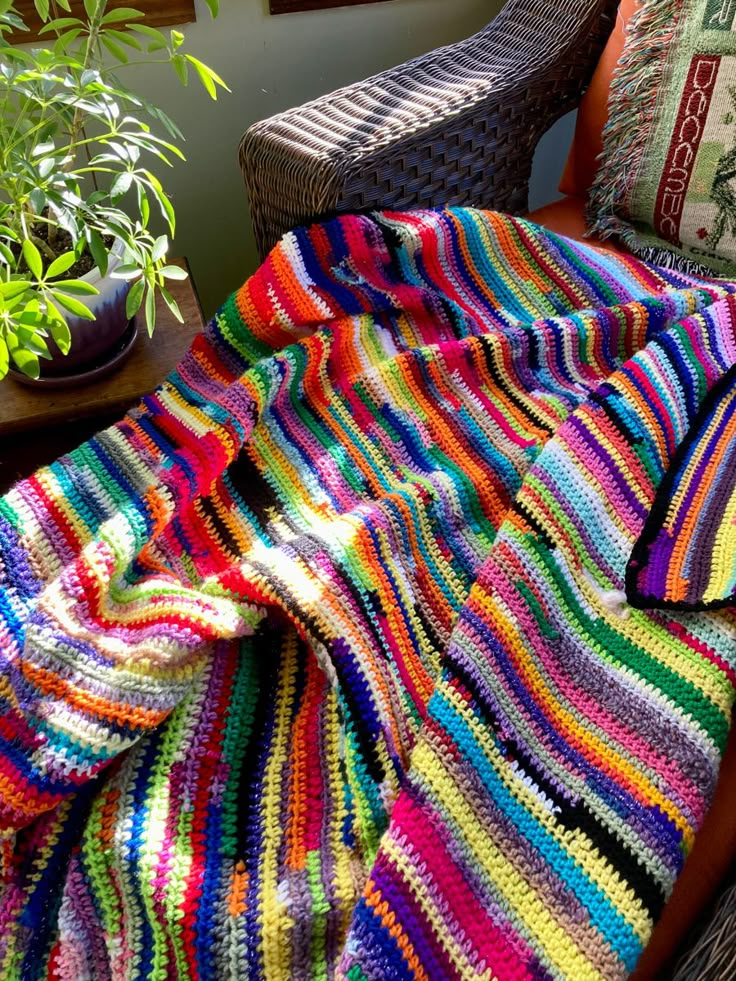 a multicolored crocheted blanket sitting on top of a chair next to a potted plant