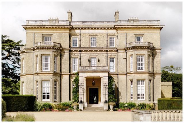 a large building with lots of windows and plants on the front lawn, surrounded by hedges