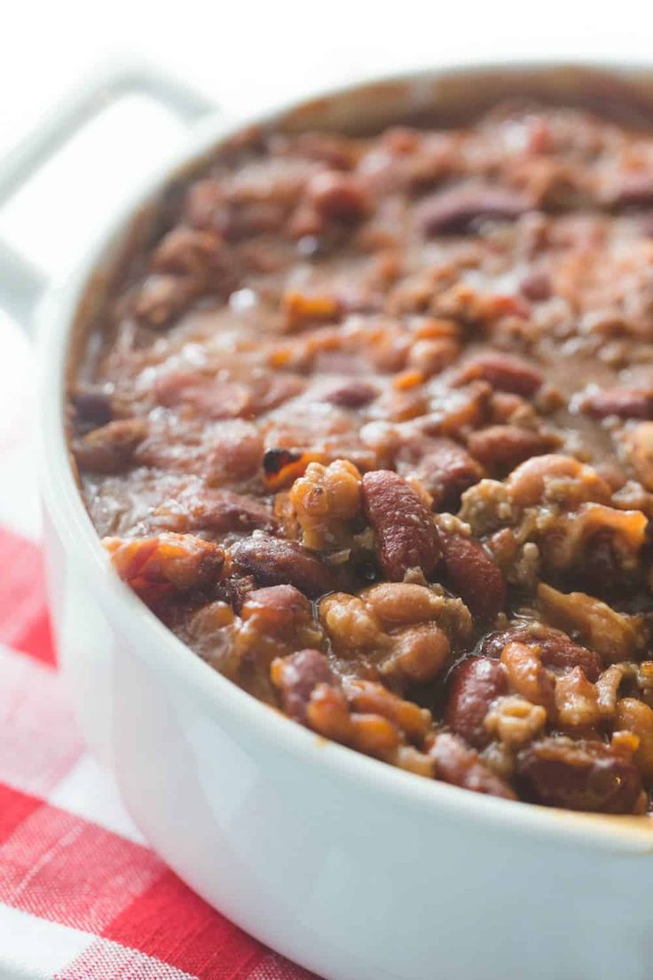 a white bowl filled with beans and meat on top of a red checkered table cloth