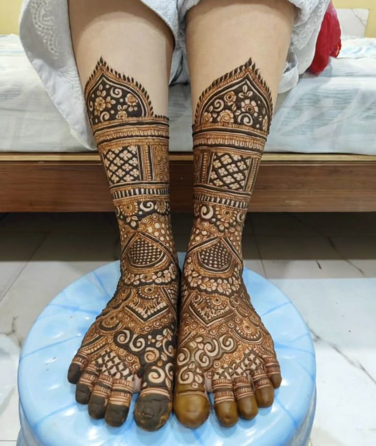 the legs and feet of a woman with henna tattoos on their hands, sitting on top of a blue stool