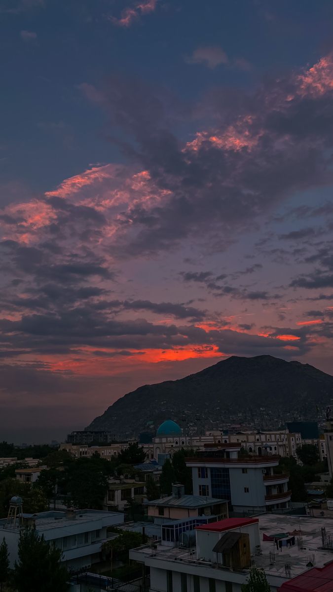 the sun is setting over a city with mountains in the backgrouund and clouds in the sky