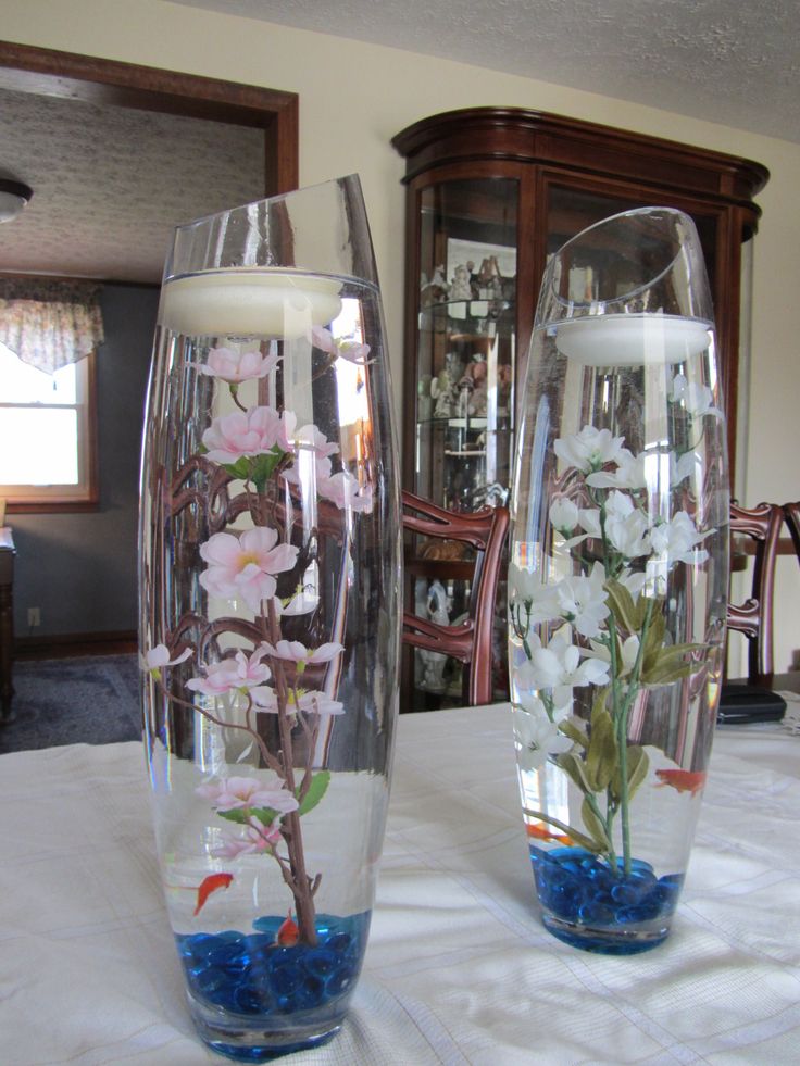 two clear vases with flowers in them sitting on a white tablecloth covered table