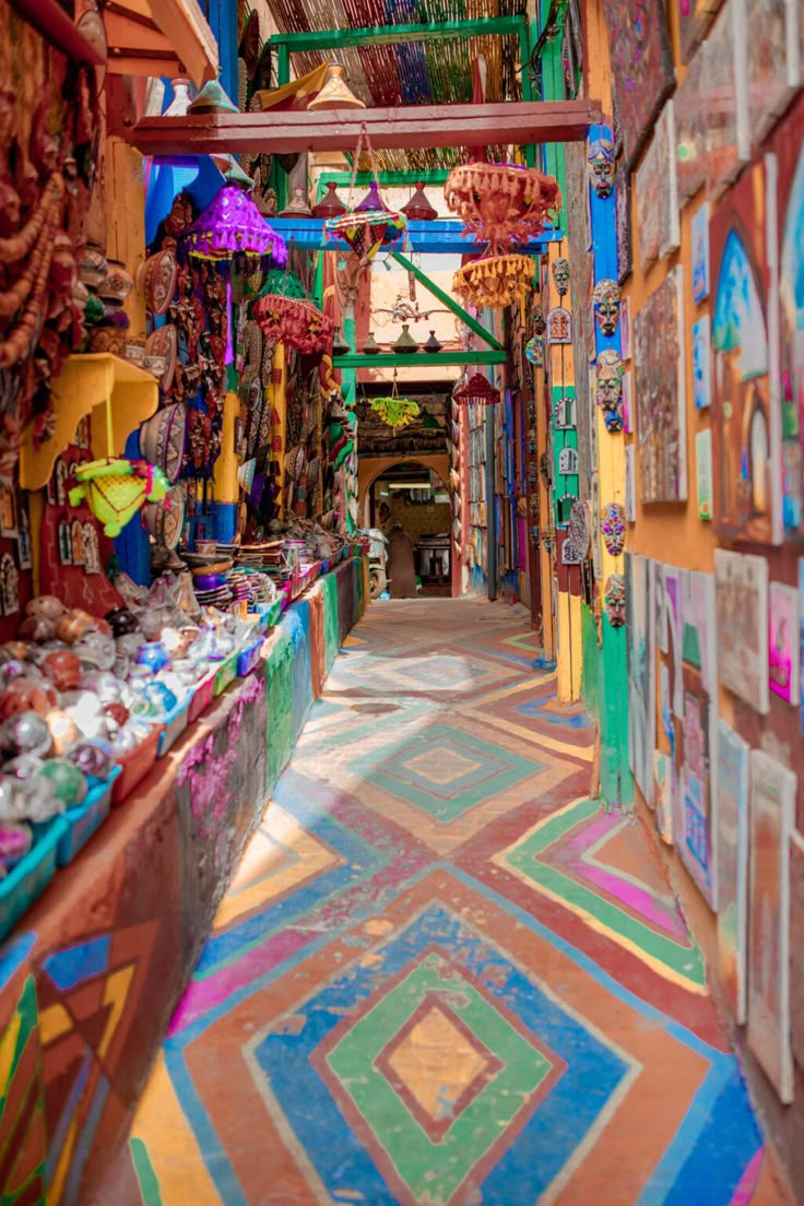 an alley way with lots of colorful paintings on the walls and ceiling, along with hanging lights