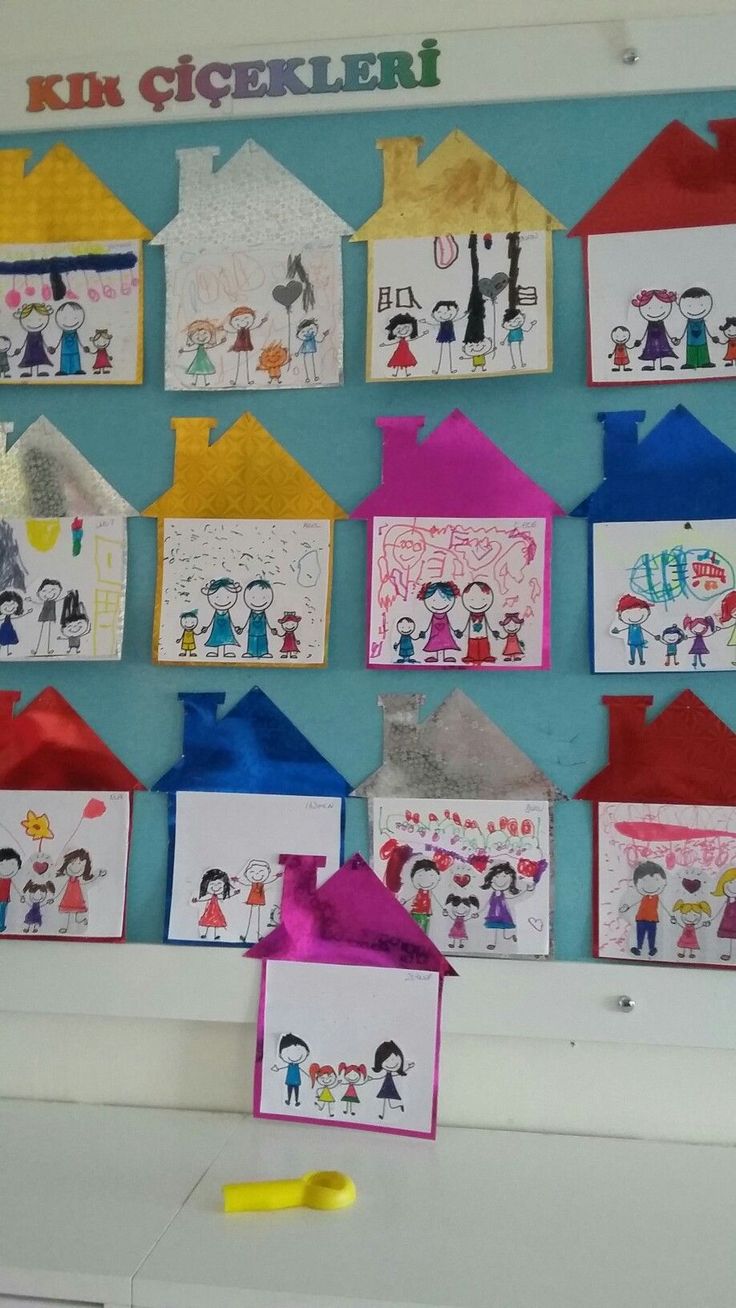 a bulletin board with children's drawings on it and paper houses hanging from the wall