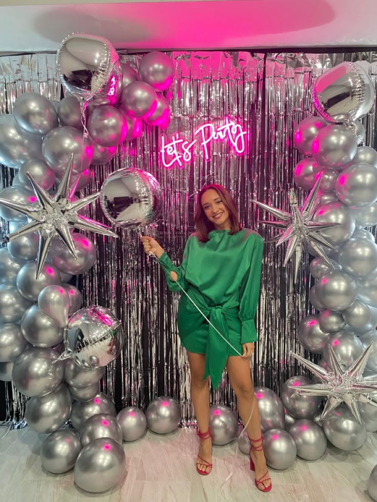 a woman standing in front of a backdrop with silver balloons and star shaped decorations on it