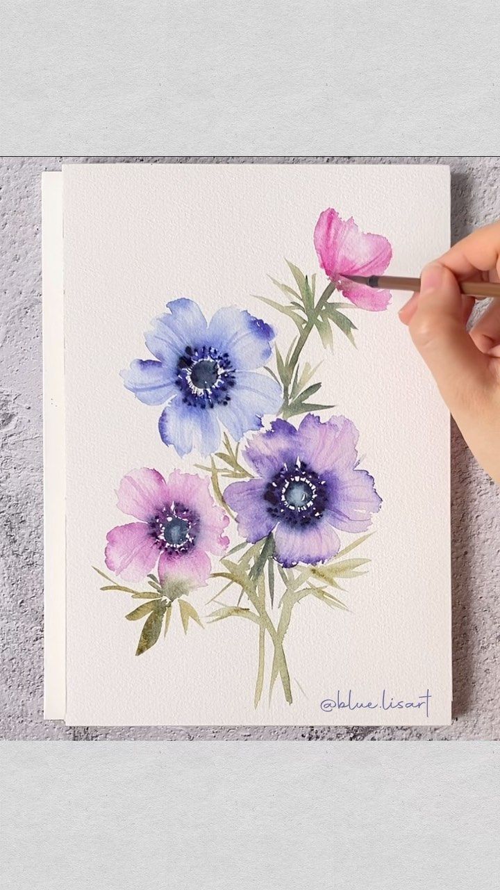 a person is painting flowers with watercolors on the paper and holding a brush