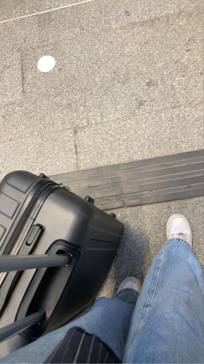 a person standing next to a black piece of luggage on top of a sidewalk with their feet propped up