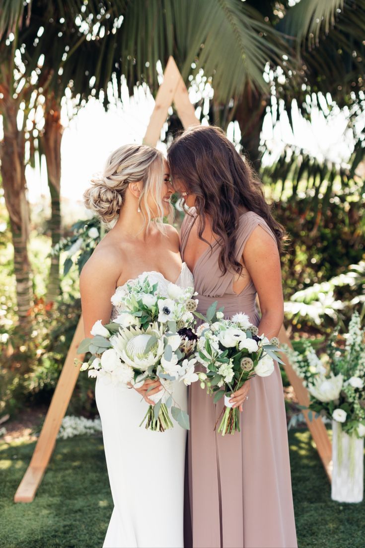 two women standing next to each other in front of palm trees and holding bouquets