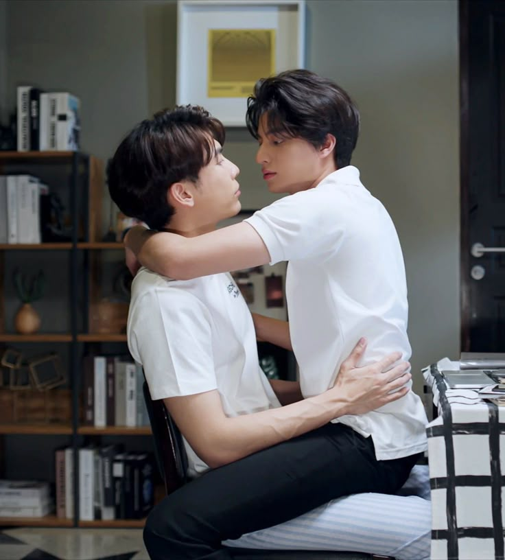 two young men hugging each other while sitting at a desk