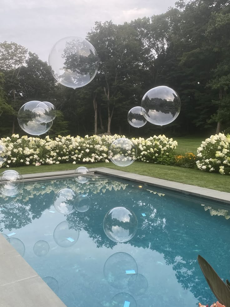 soap bubbles floating in the air over a swimming pool with flowers and bushes behind it