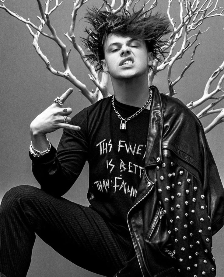 black and white photograph of a young man sitting in front of a tree with his hands on his hips