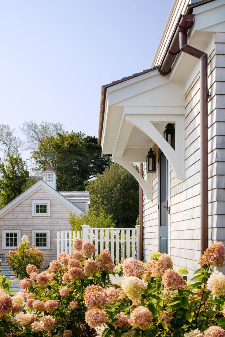 a white house with pink flowers in the foreground and a white picket fence behind it