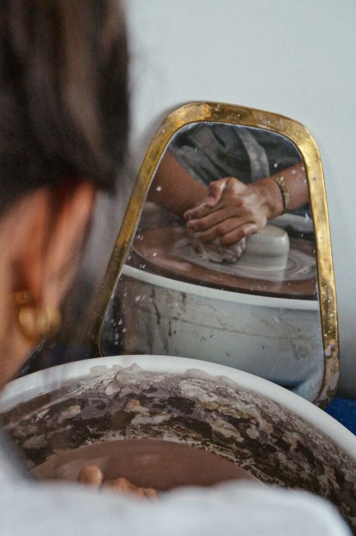 a woman is looking at her reflection in the mirror while making pottery on a wheel