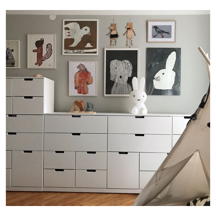 a white dresser topped with lots of drawers next to a wall covered in pictures and art