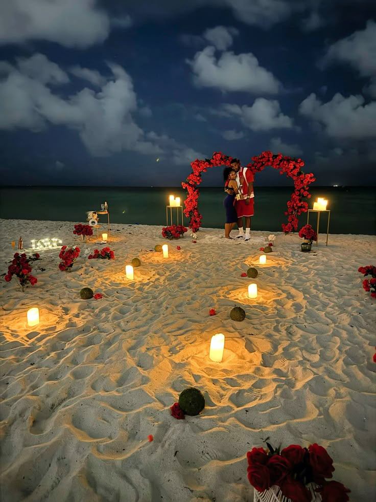 a couple standing on top of a sandy beach next to candles