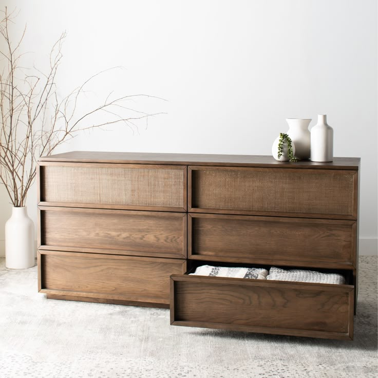 a large wooden dresser with drawers and vases on it's top shelf, in front of a white wall