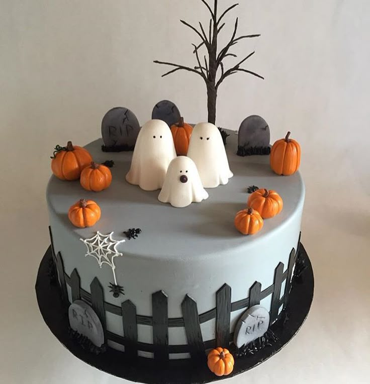 a decorated cake with ghost decorations and pumpkins on the top, sitting in front of a tree