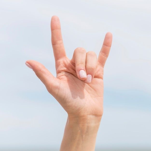 a woman's hand making the v sign with her fingers against a blue sky